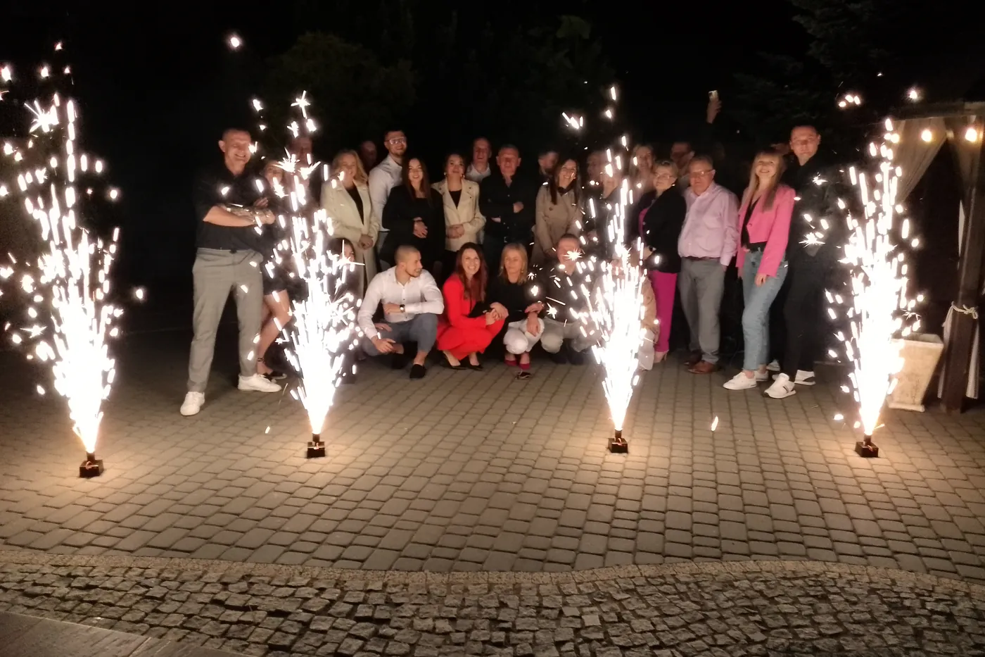 Goście pozują nocą przed rzędem fontann iskier